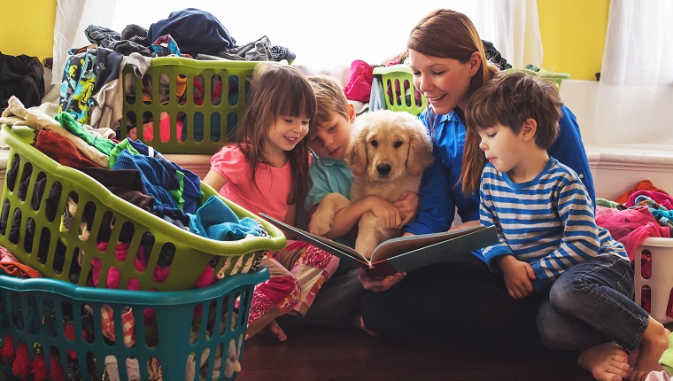 Smiling mother reading to three children and golden retriever puppy dog surrounded by laundry baskets