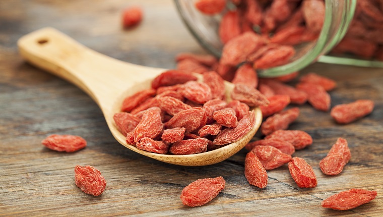 Tibetan goji berries (wolfberry) spilling of the glass jar on a wooden spoon, selective focus