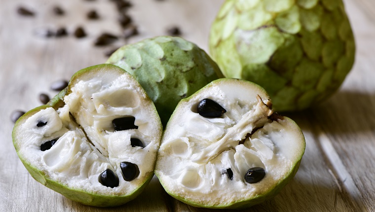 closeup of some custard apples, one of them cut in half, on a rustic wooden surface