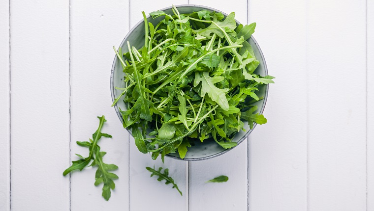 Bowl with fresh green salad arugula rucola on a wooden Black or White background