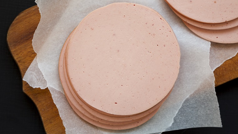 Sliced pork bolgna meat on a rustic wooden board on a black surface, top view. Flat lay, overhead, from above.