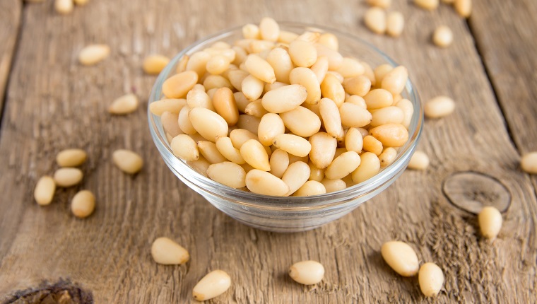 Pine nuts tasty, fresh, in glass bowl on wooden background (table) close up, horizontal