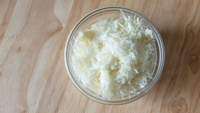 Bowl of grated Pecorino Romano cheese. Wooden surface. High point of view.