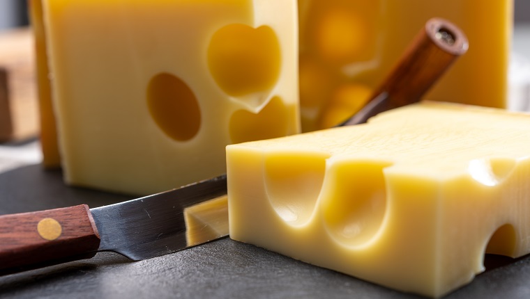 Block of Swiss medium-hard yellow cheese emmental or emmentaler with round holes and cheese knife close up