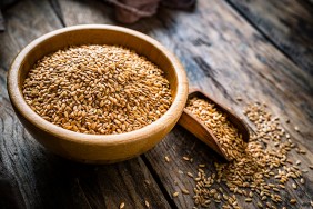 Healthy food: high angle view of a brown bowl filled with flax seeds on a rustic wooden table. A wooden serving scoop is beside the bowl and some seeds spilled out. The composition is at the left of an horizontal frame leaving useful copy space for text and/or logo at the right. Predominant color is brown. High resolution 42Mp studio digital capture taken with SONY A7rII and Zeiss Batis 40mm F2.0 CF lens