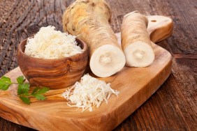 Fresh and grated horseradish in wooden bowl with parsley on wooden cutting board. Horse-radish root.