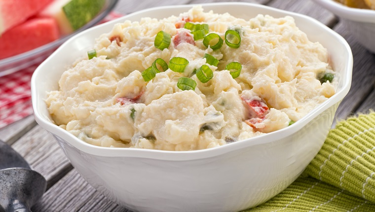 A delicious homemade creamy potato salad on a rustic picnic table.