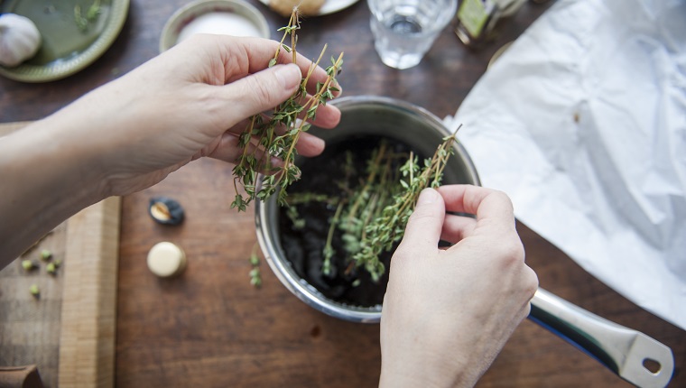 Woman adding fresh thyme leaves to a cooking pot filled with balsamic vinegar, to make a dressing. First person perspective.