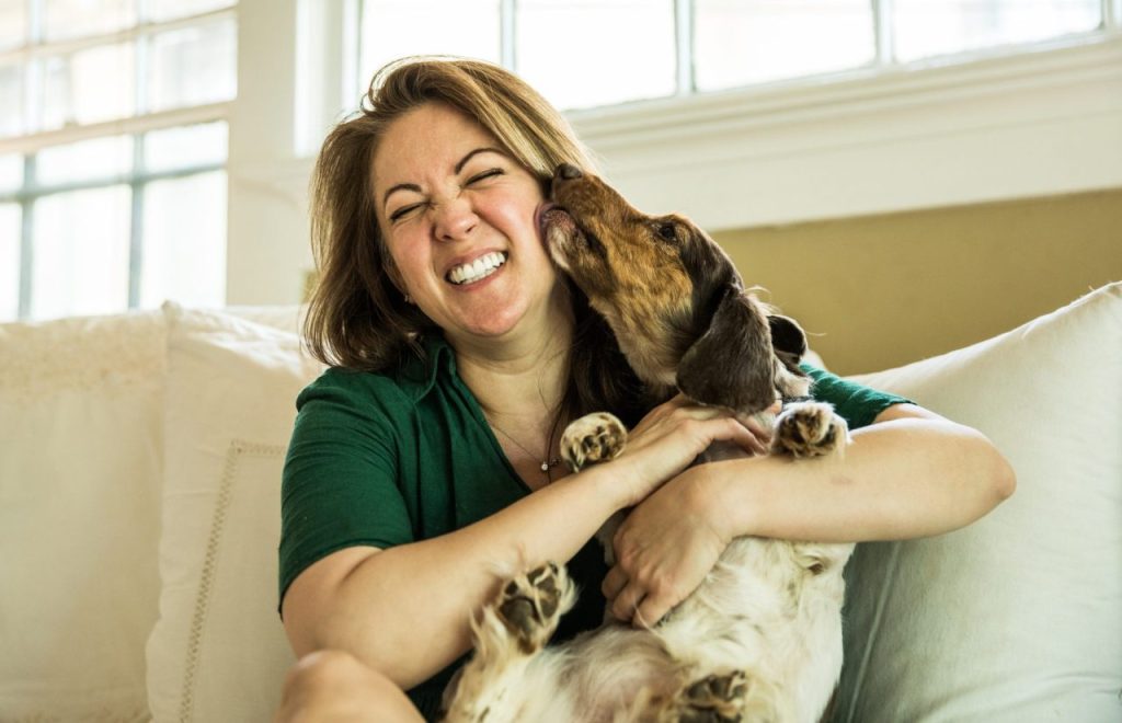 Woman hugging a foster dog on her couch in her home.