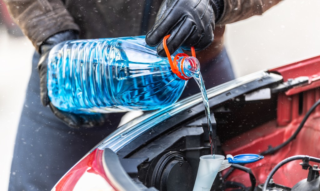 A male driver wearing gloves pours antifreeze into the tank to spray the windshield during a snowstorm.