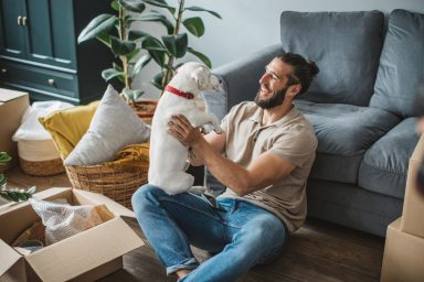 Young man moving in pet-friendly apartment. He is happy and playing with his pet dog.