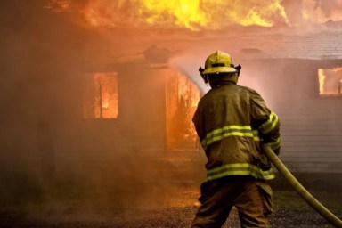 Firefighter spraying water at a house fire.