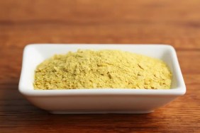 A closeup photo of yellow nutritional yeast in a white ceramic dish. Nutritional yeast can be safe for dogs to eat.