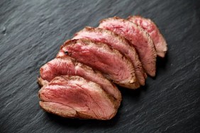 Mediium-rare cooked venison meat on a cutting board, which dogs an eat safely when cooked.