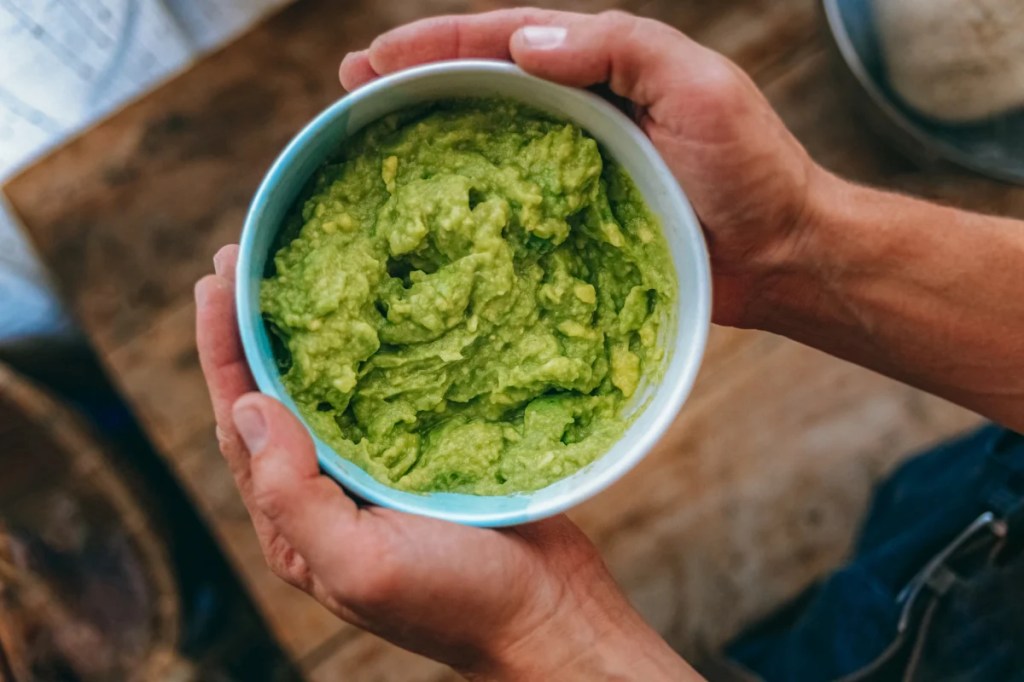 Photograph of a man's hands holding a bowl of guacamole, which is not safe for dogs to eat.