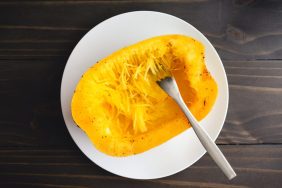 Seeded and cooked half of spaghetti squash being shredded with a fork