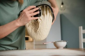 A photo of a woman making fresh bread. She dumps out bread dough, containing baking yeast which is dangerous to dogs.