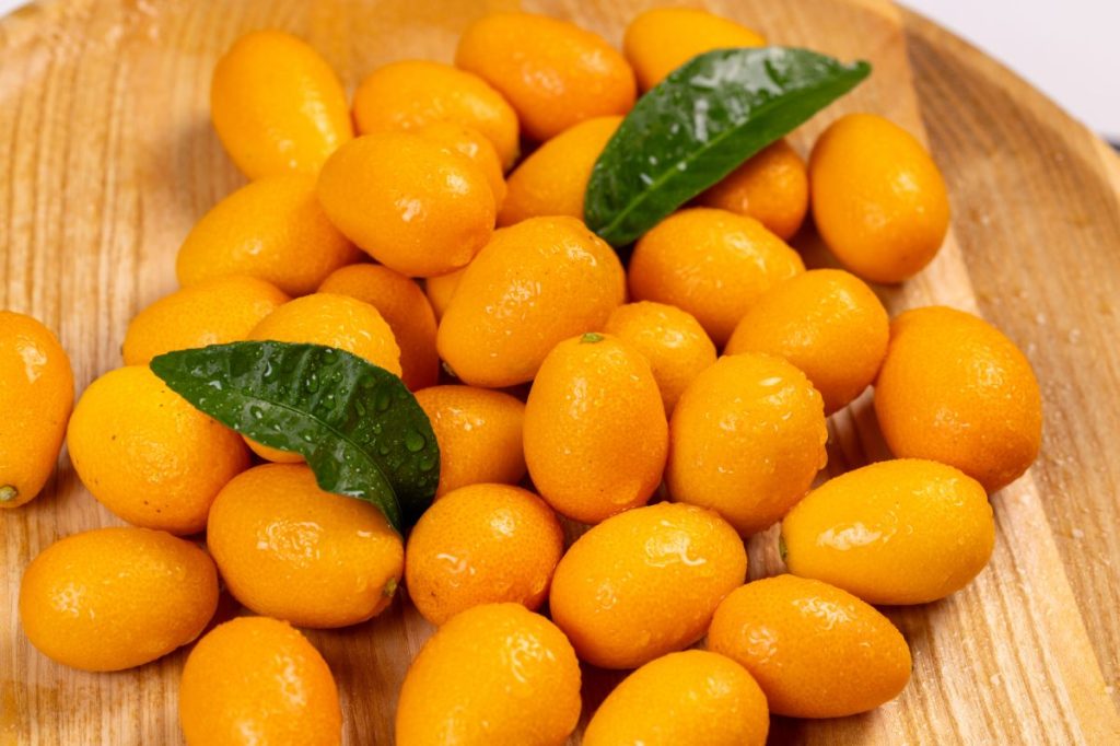 Vibrant kumquats with green leaves, creating a colorful display on a wooden surface, ideal for food and drink projects