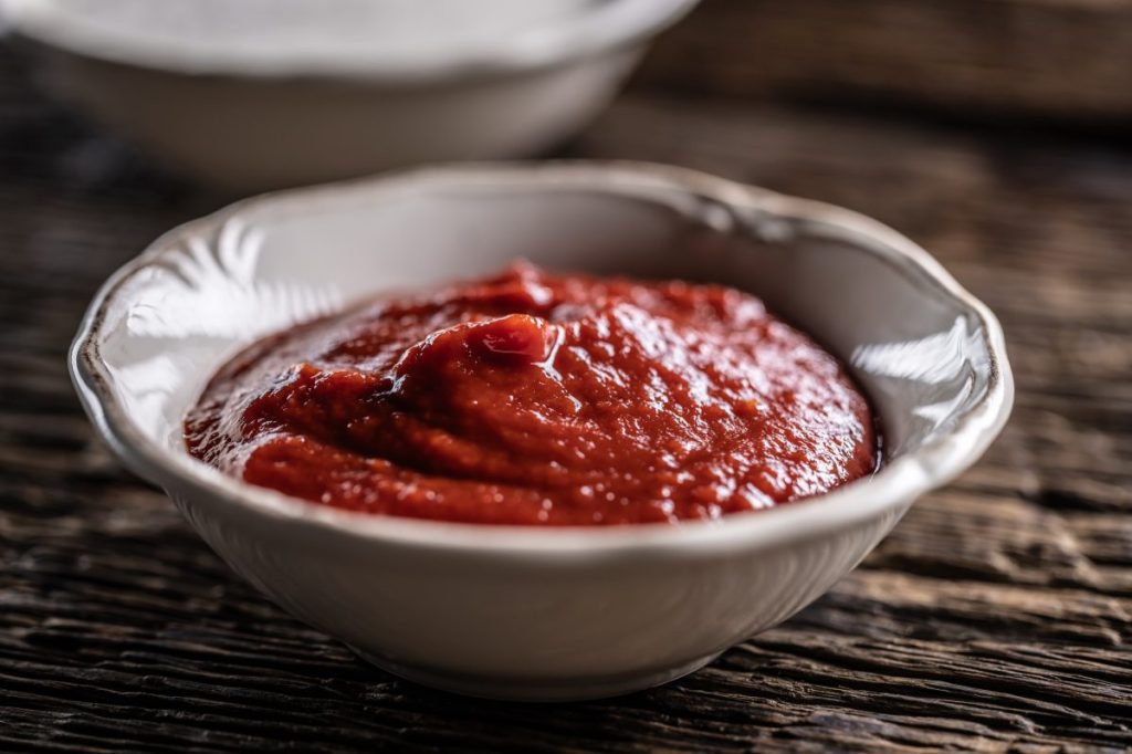 A closeup shot of tomato ketchup in a white ceramic bowl. Dogs can eat ketchup in small amounts, provided it is does not include garlic or onion powder or added sugars.