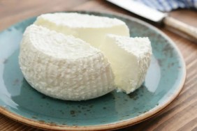 A close-up photo of fresh ricotta cheese, which can be safe for dogs to eat in moderation, on a blue ceramic plate.