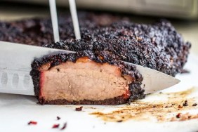 A closeup photo of a knife slicing through smoked brisket, which dogs can eat provided its free of seasonings containing onion and garlic. Always feed in moderation.